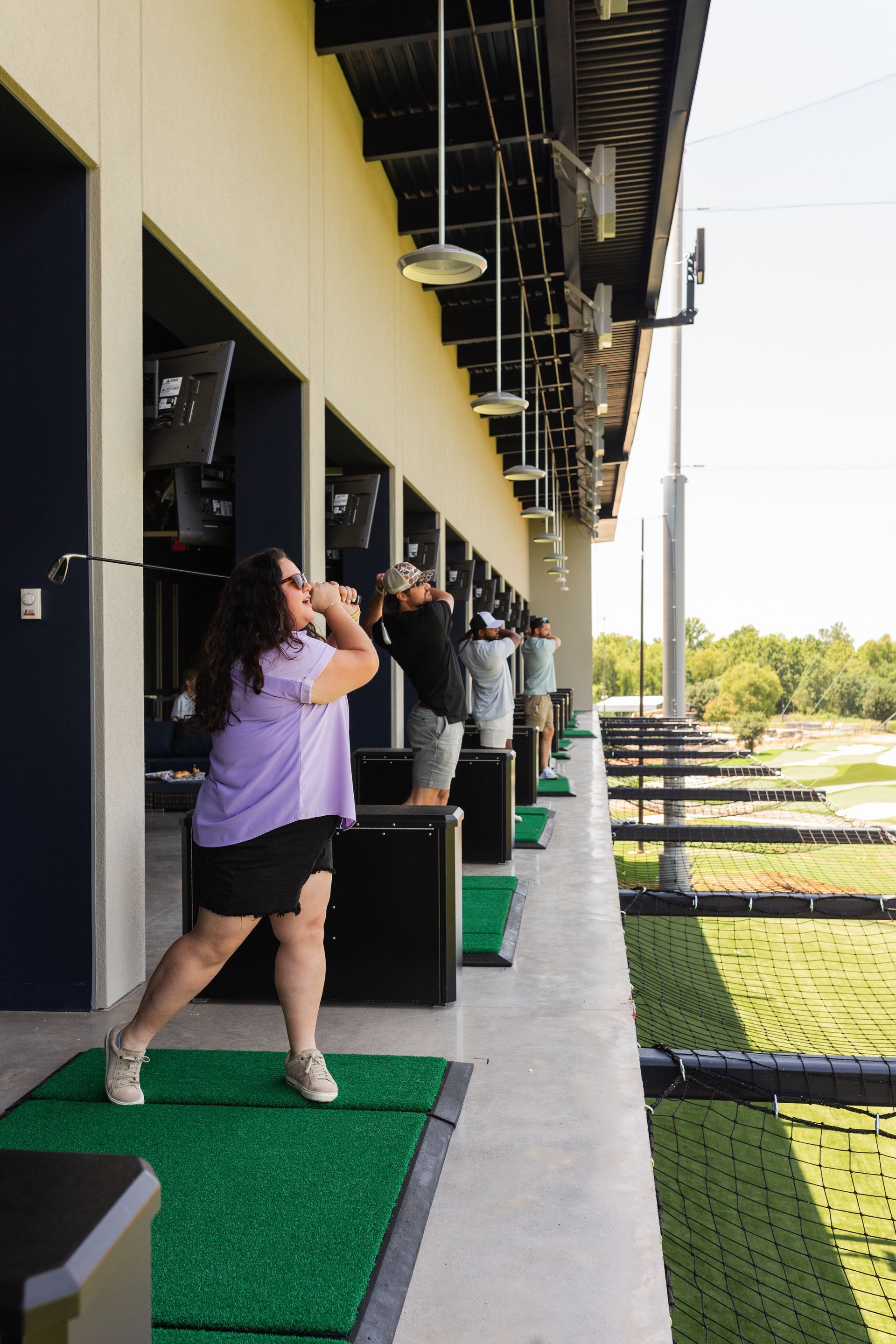 People practicing golf swings at a driving range under a covered bay outdoors
