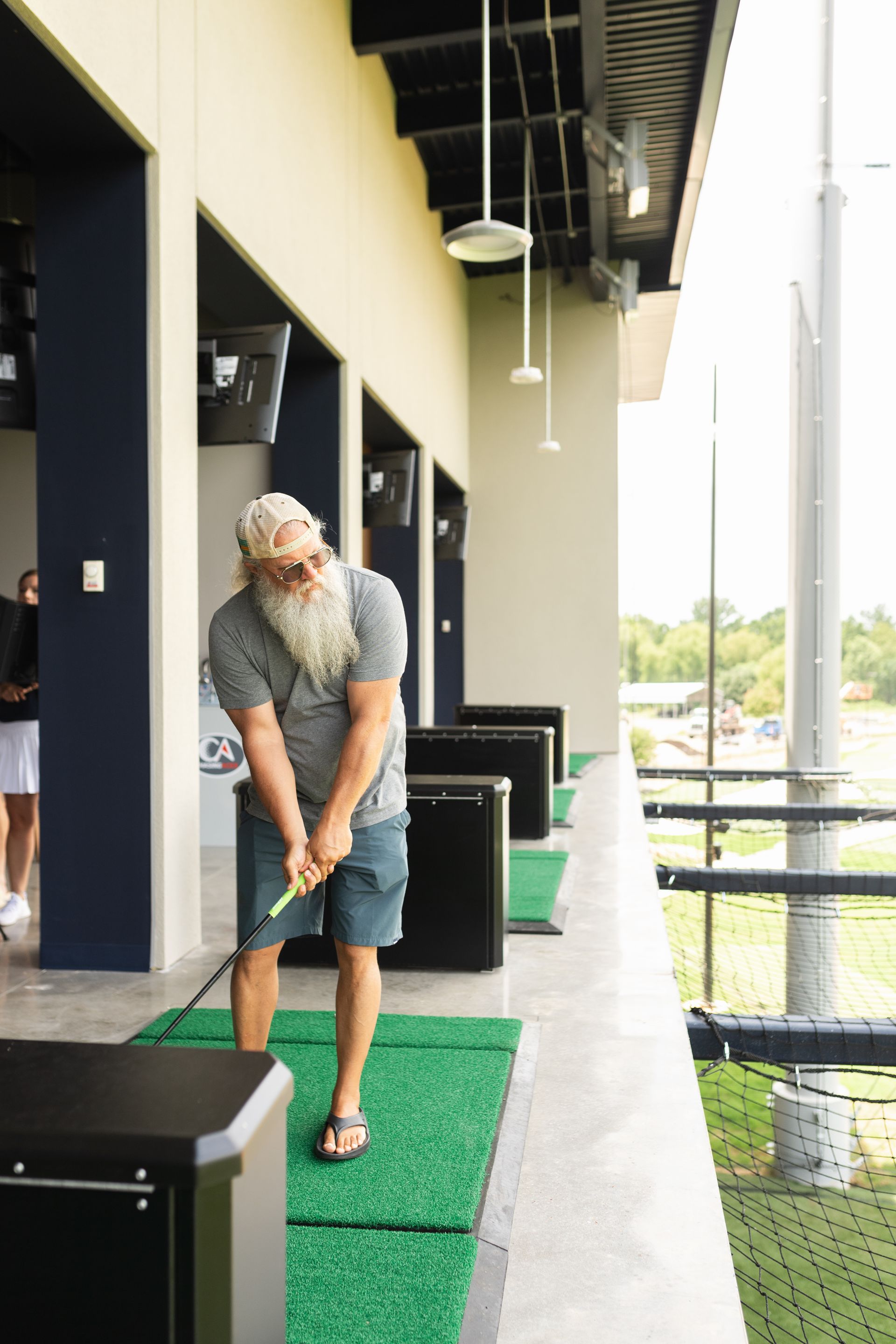 A man with a beard is swinging a golf club at a golf course.