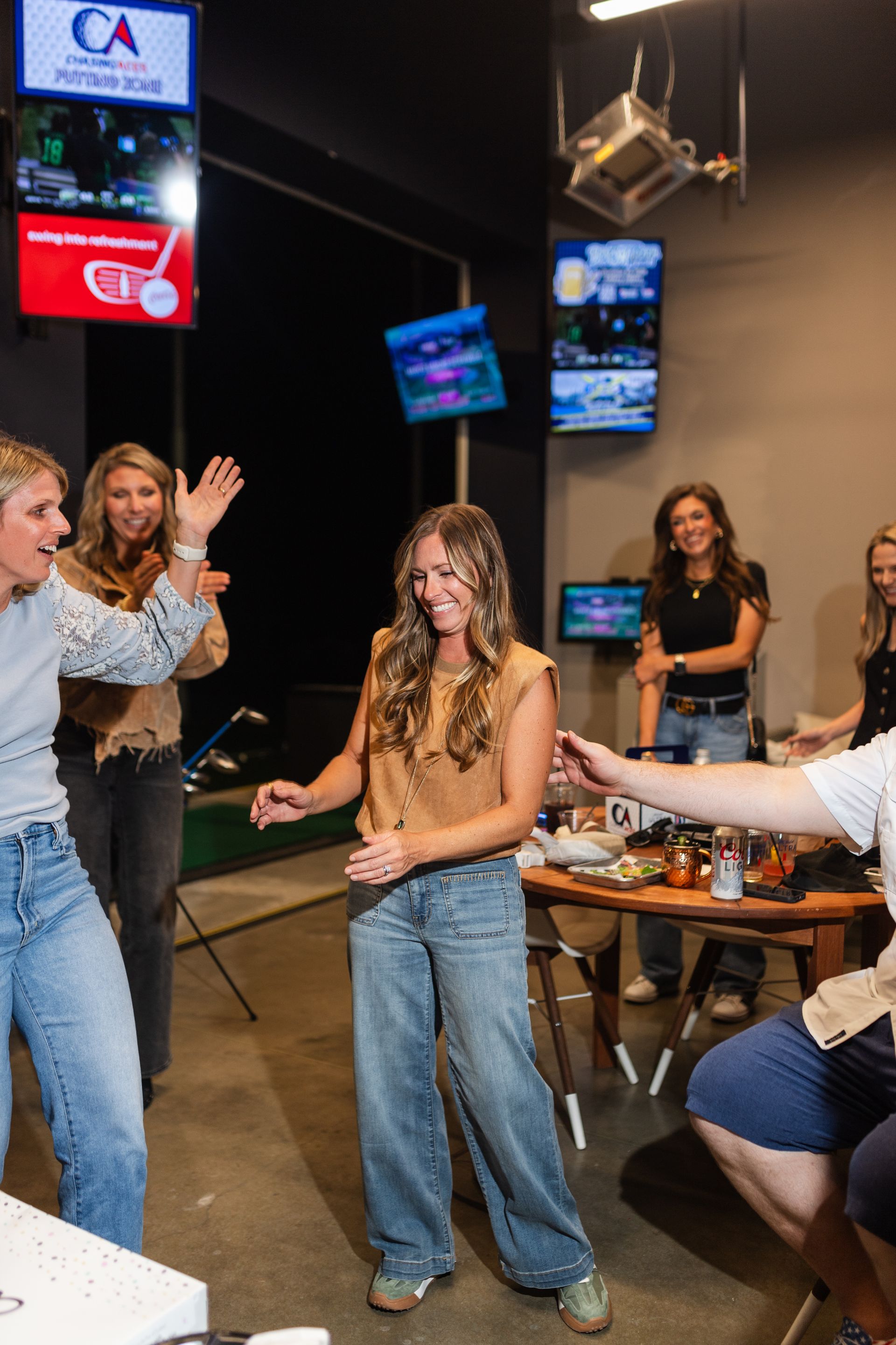 People dancing and laughing in a simulated golf setting, with screens displaying golf-related content.