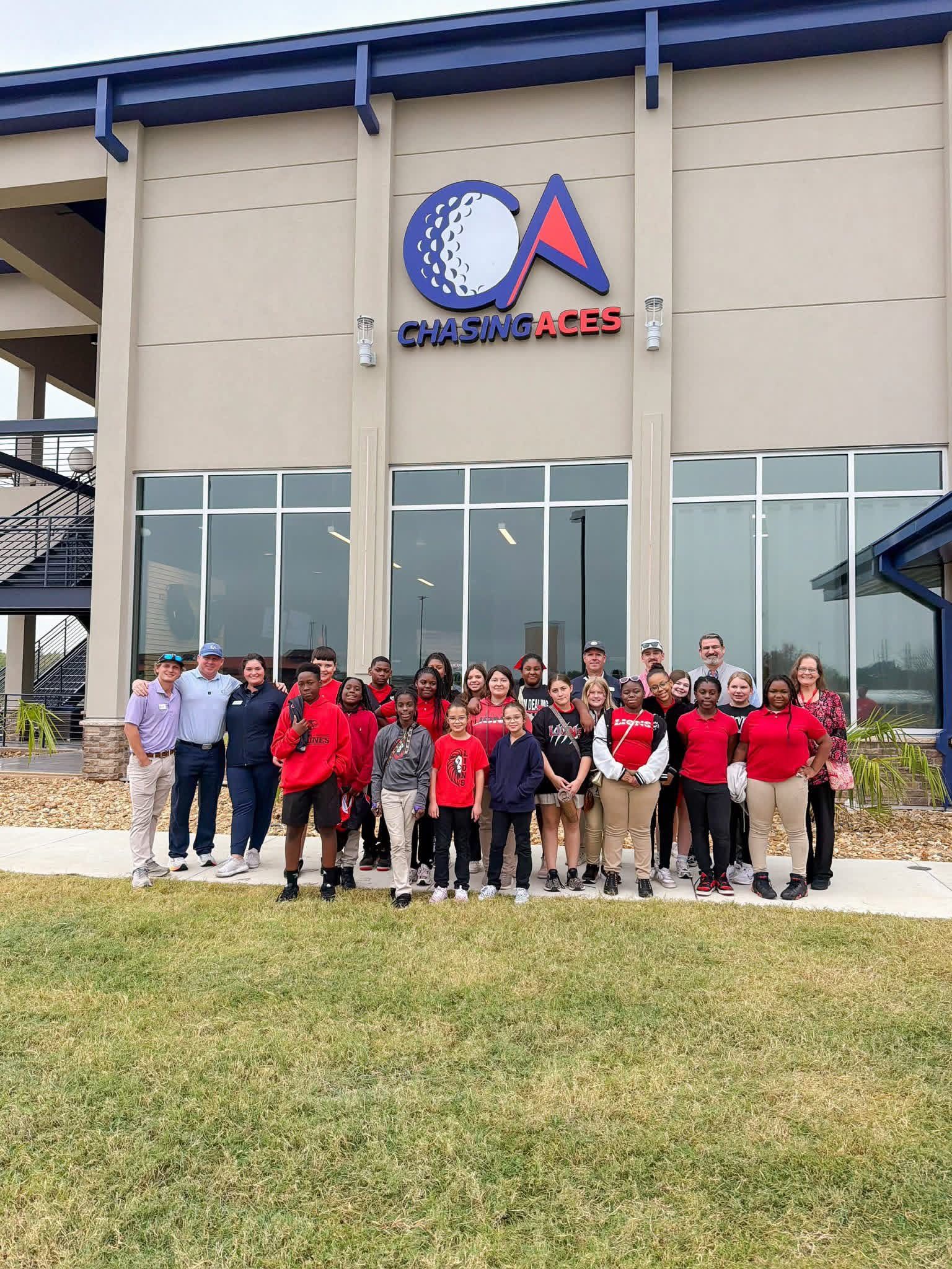 A group of people standing outside a Chasing Aces golf facility, smiling and posing for a photo.