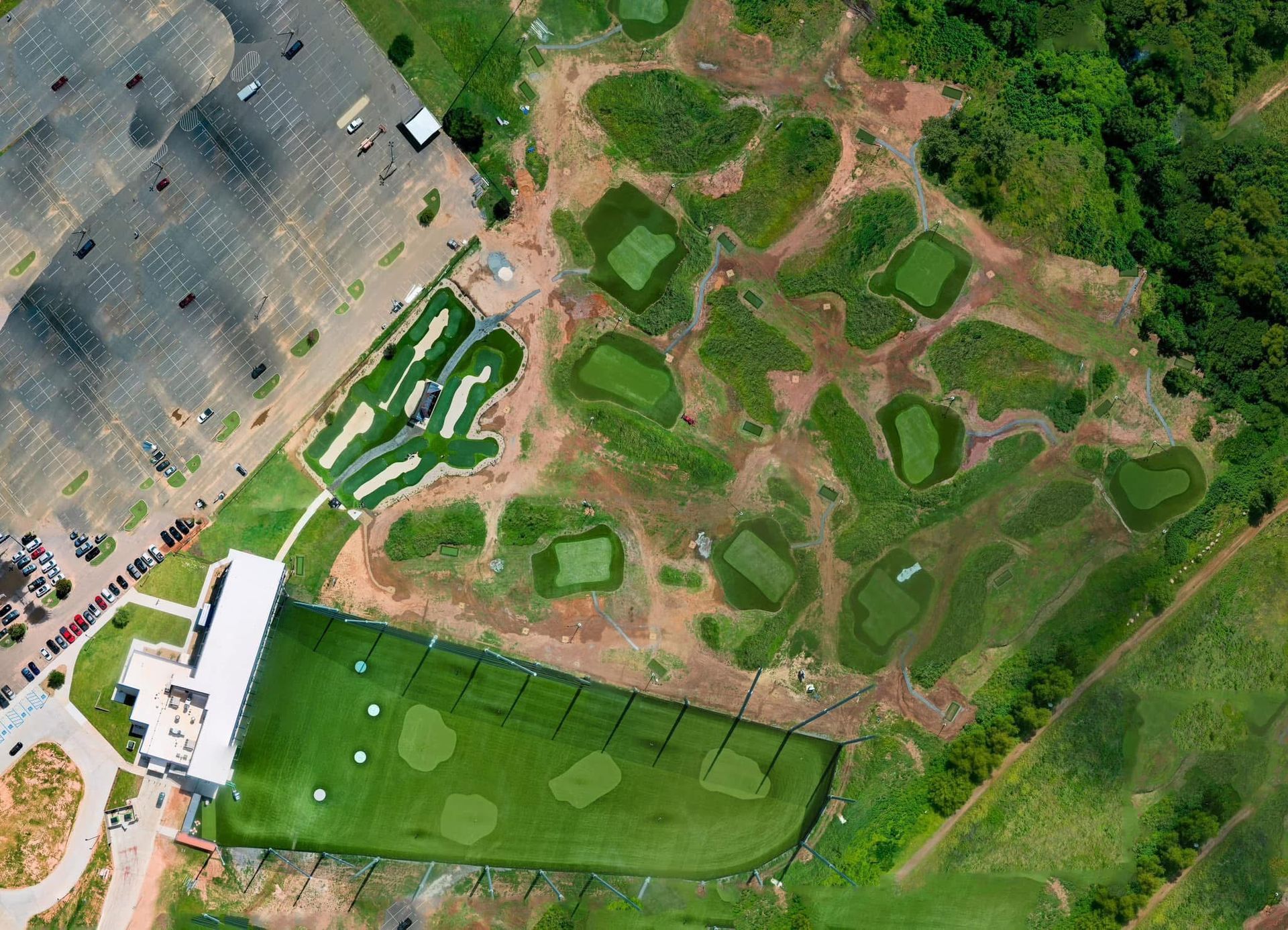 Aerial view of a golf driving range with a building, parking lot, and multiple target greens set in a field.