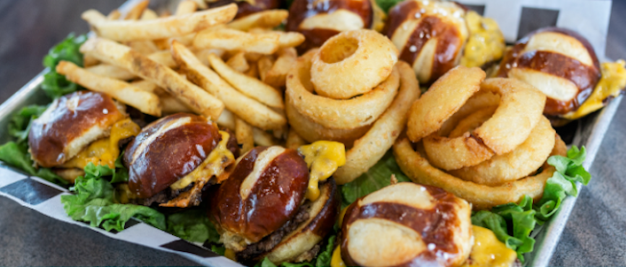 Loaded tray of sandwiches topped with melted cheese, fries, onion rings, and lettuce