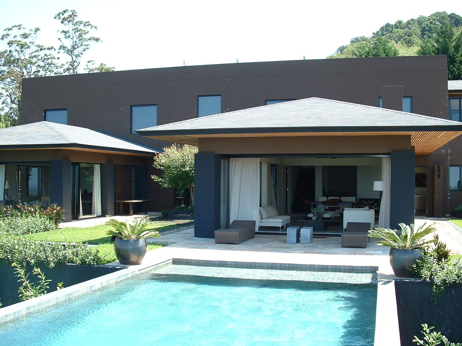Poolside view of a modern house with a pool, patio, and two detached structures with green landscaping — South Coast Glass In South Nowra, NSW