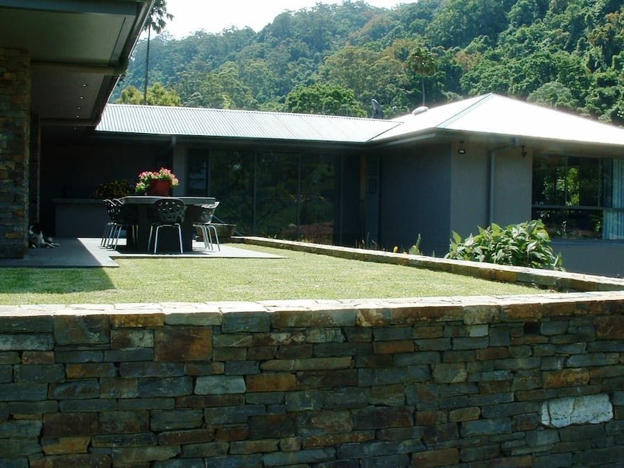 A Stone Wall Surrounds A Lush Green Lawn In Front Of A House — South Coast Glass In South Nowra, NSW