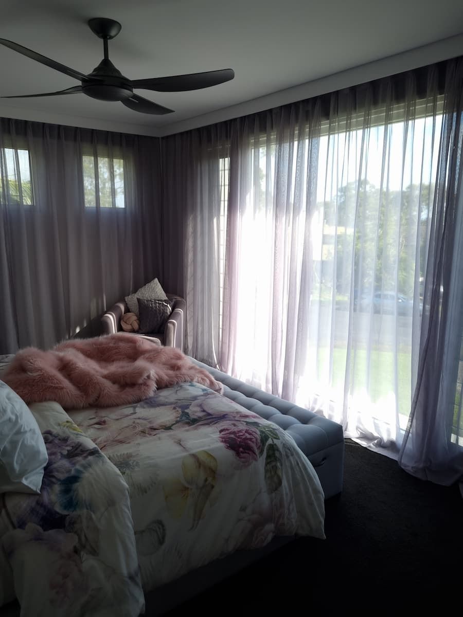 A Bedroom With A Bed, Chair, Ceiling Fan And Sheer Curtains — South Coast Glass In South Nowra, NSW