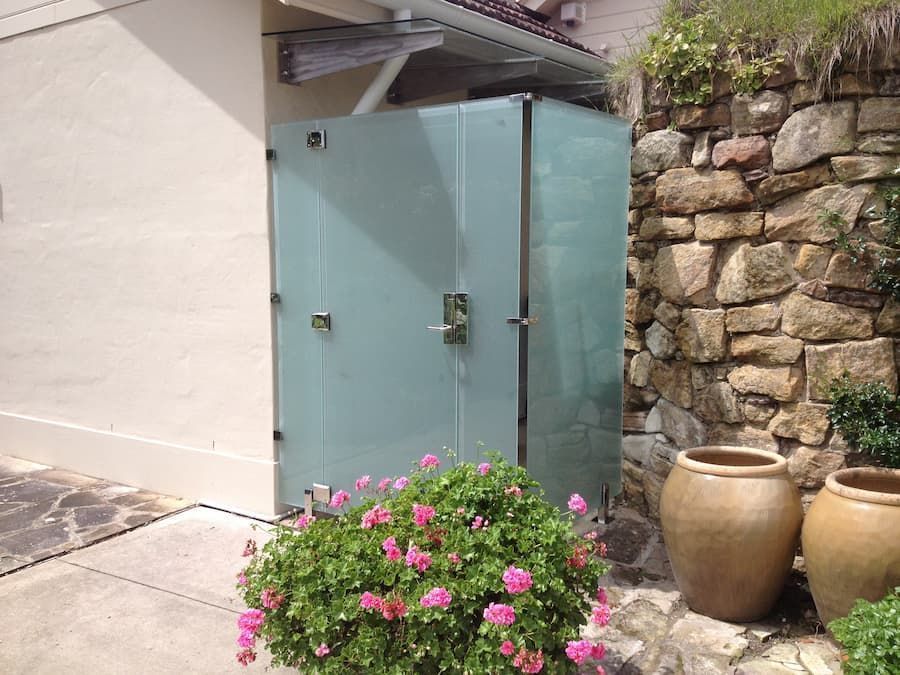 A Glass Door Is Surrounded By Potted Plants And Flowers In Front Of A Stone Wall — South Coast Glass In South Nowra, NSW