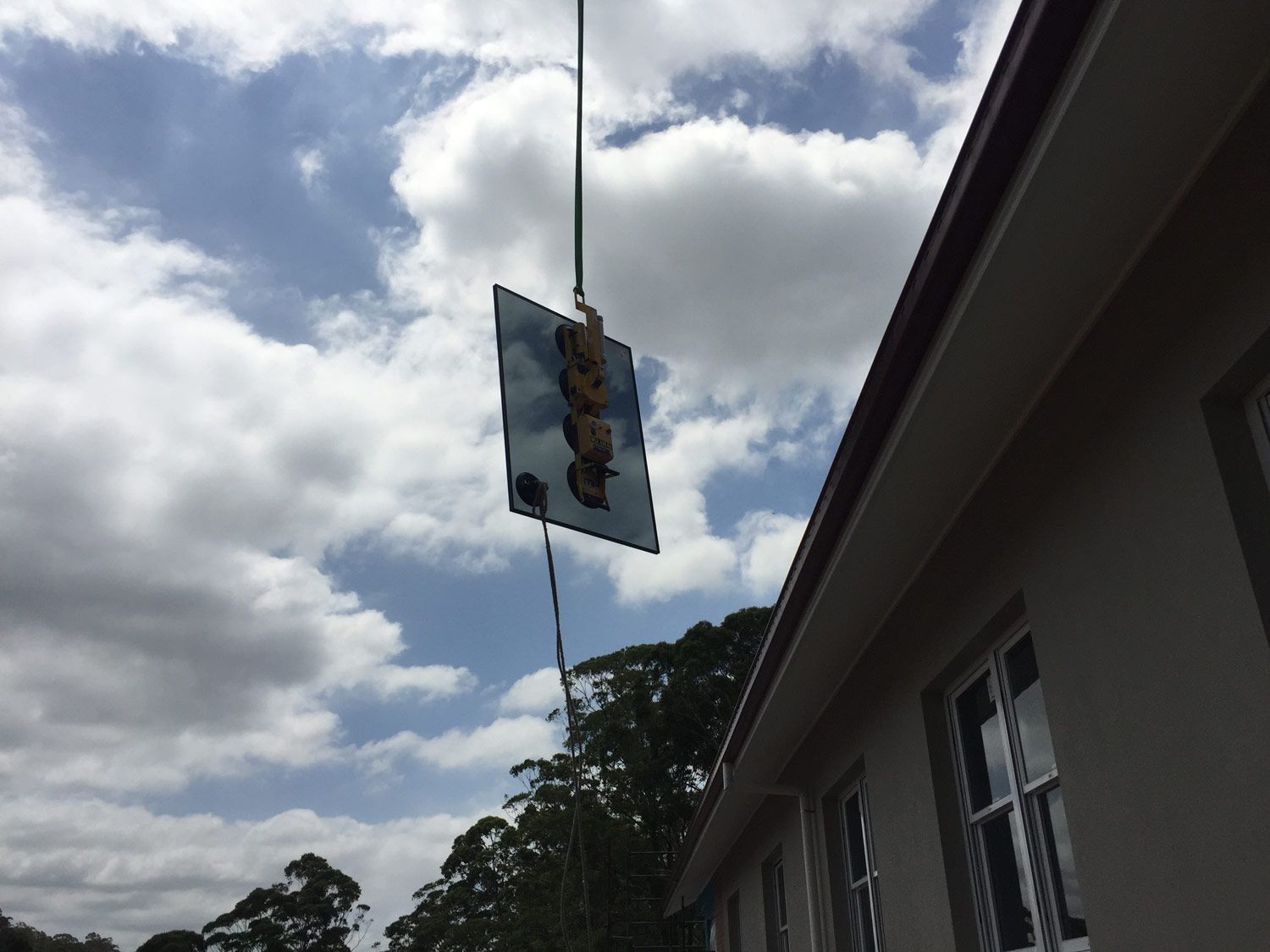 A Crane is Holding Small Piece of Glass Towards the Window Frame — South Coast Glass In South Nowra, NSW