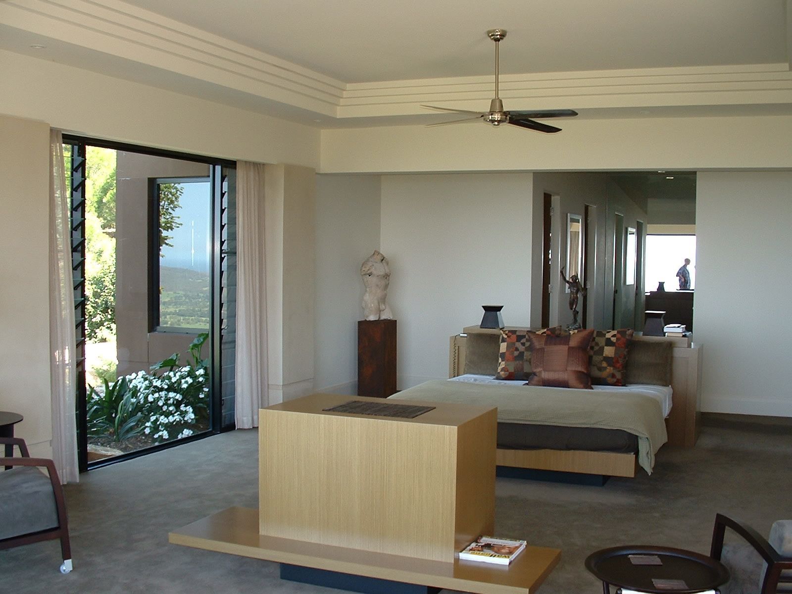 Spacious bedroom with sliding glass door, flowers outside, and modern furniture in muted tones — South Coast Glass In South Nowra, NSW