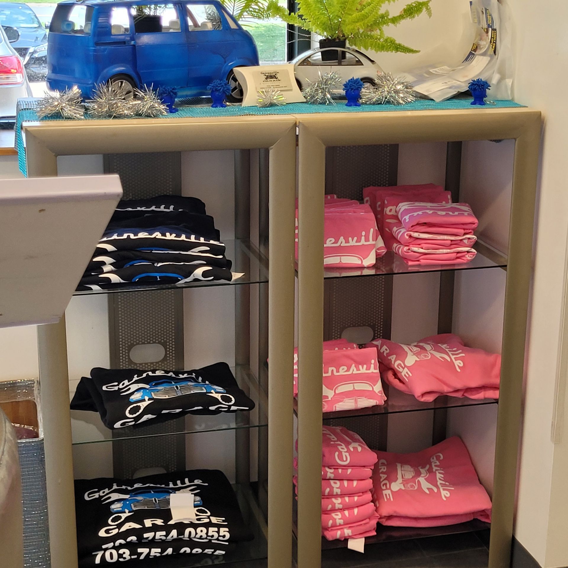 Display case with stacked black and pink t-shirts; decorated top shelf with a blue van model. | Gainesville Garage & Trailer Sales