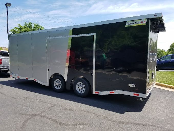 Silver and black enclosed trailer parked on asphalt under a bright sky. | Gainesville Garage & Trailer Sales