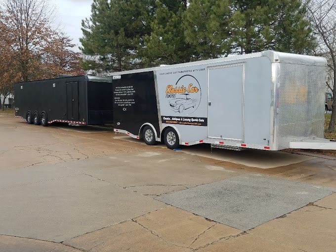 Two connected semi-truck trailers; black and silver, parked on pavement, with a logo visible on the silver trailer. | Gainesville Garage & Trailer Sales