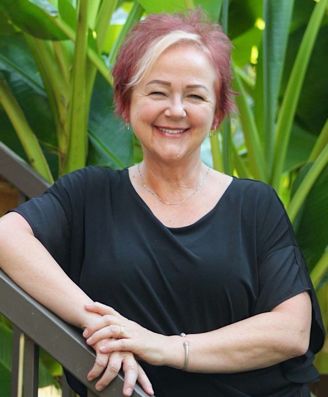 A woman in a black shirt is leaning on a railing and smiling.