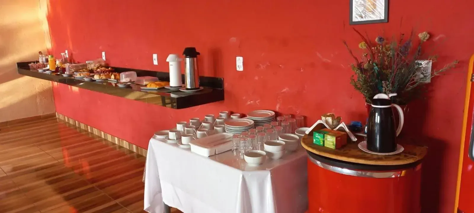 Há uma mesa com uma toalha branca e uma parede vermelha atrás dela.-Pousada-Morada-dos-Passaros