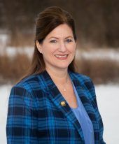 Woman in blue plaid blazer smiles, with winter backdrop.
