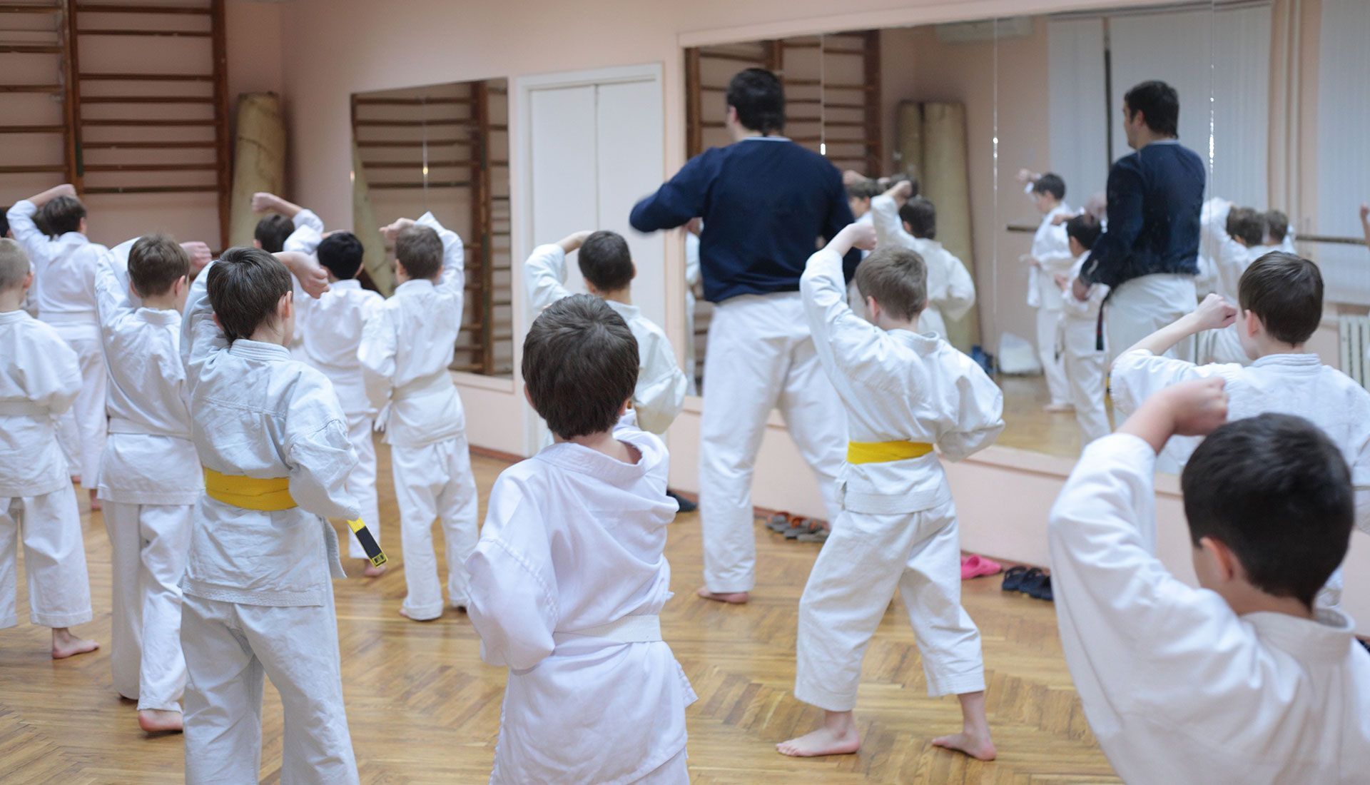 Children in white karate uniforms practice with instructors in a dojo.