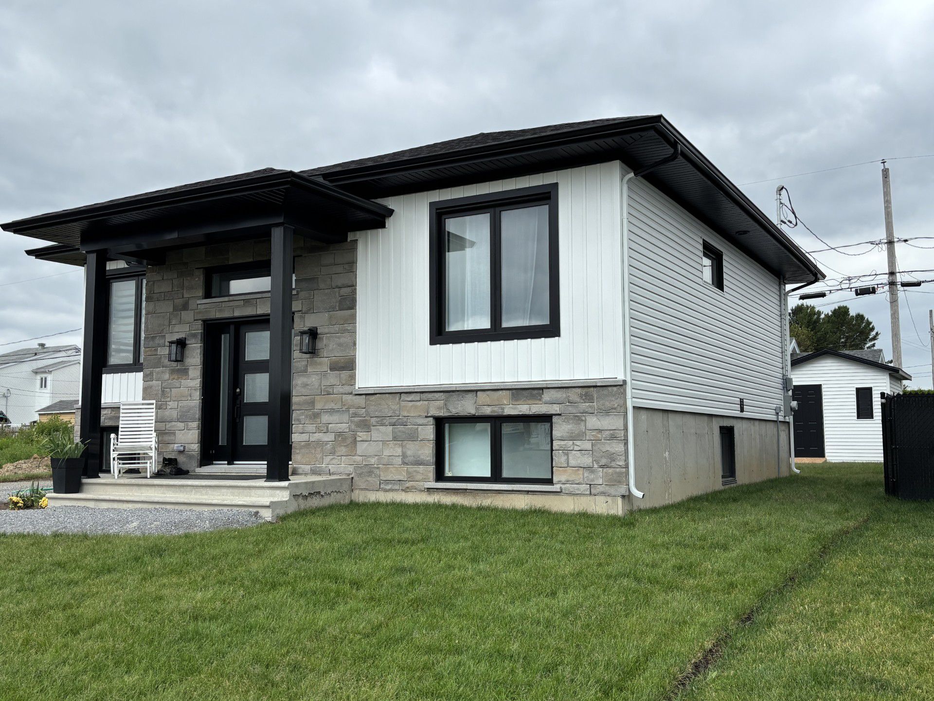 Modern white house with stone accents, a black front door, and a green lawn under a cloudy sky