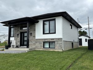 Maison blanche moderne avec des boiseries foncées et des accents de pierre sur un terrain gazonné sous un ciel couvert