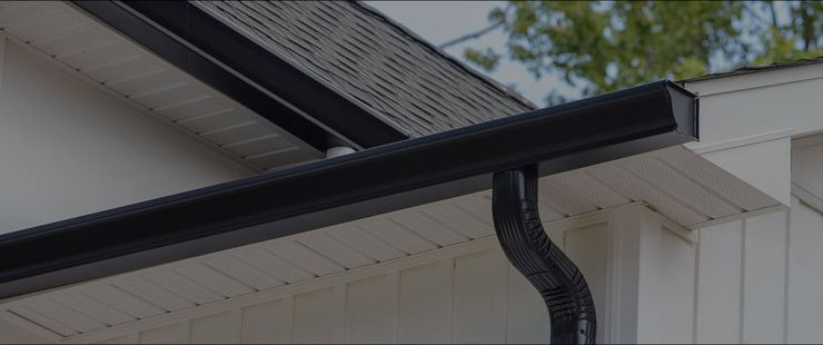 Gouttière et descente pluviale noires sur le toit d'une maison blanche sous un ciel nuageux