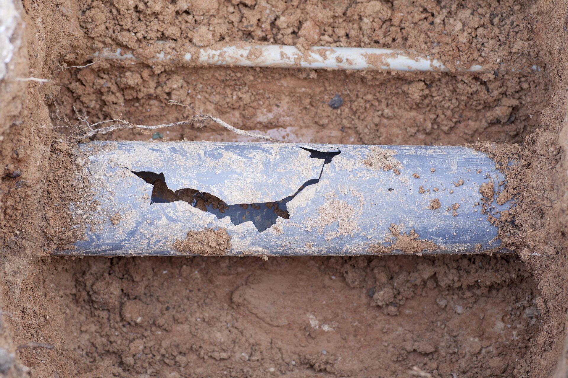 A pipe is laying in the dirt with a hole in it.