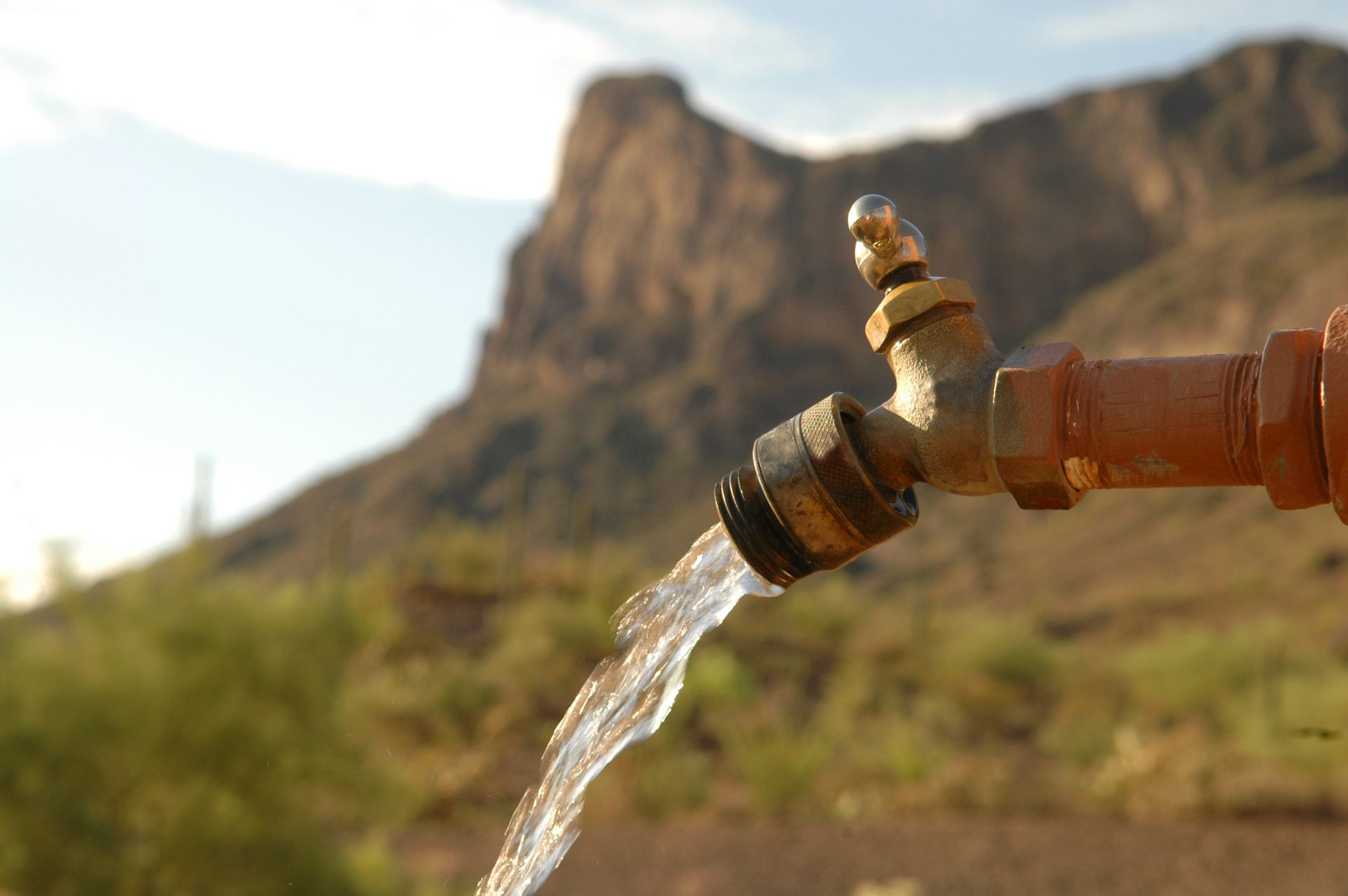 Water flowing from a metal faucet with a rocky desert cliff in the background