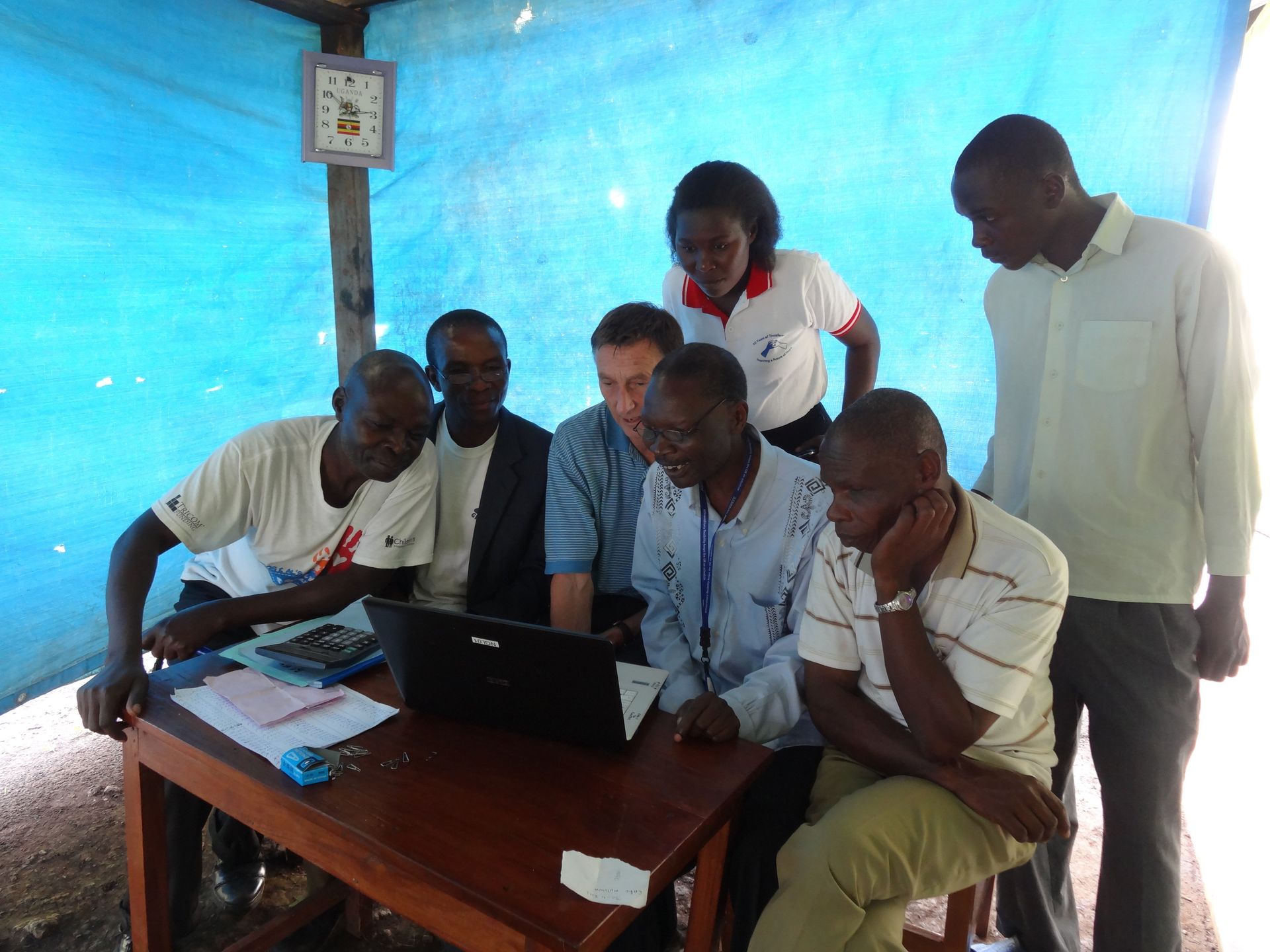 A group of people looking at a laptop, discussing inside a blue-tarped structure.