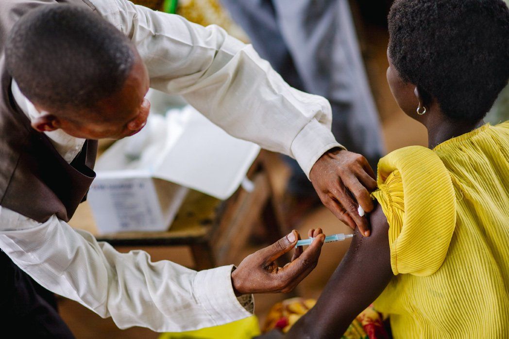 Person giving an injection to a woman's arm; vaccine being administered in a clinic setting.