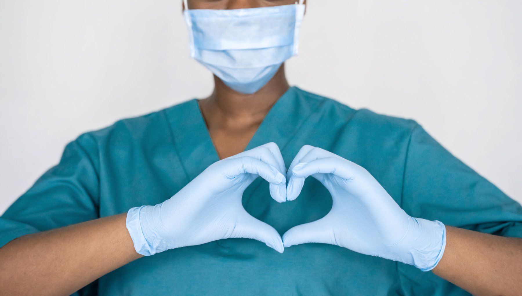 Medical professional in blue scrubs and gloves forming a heart with their hands.