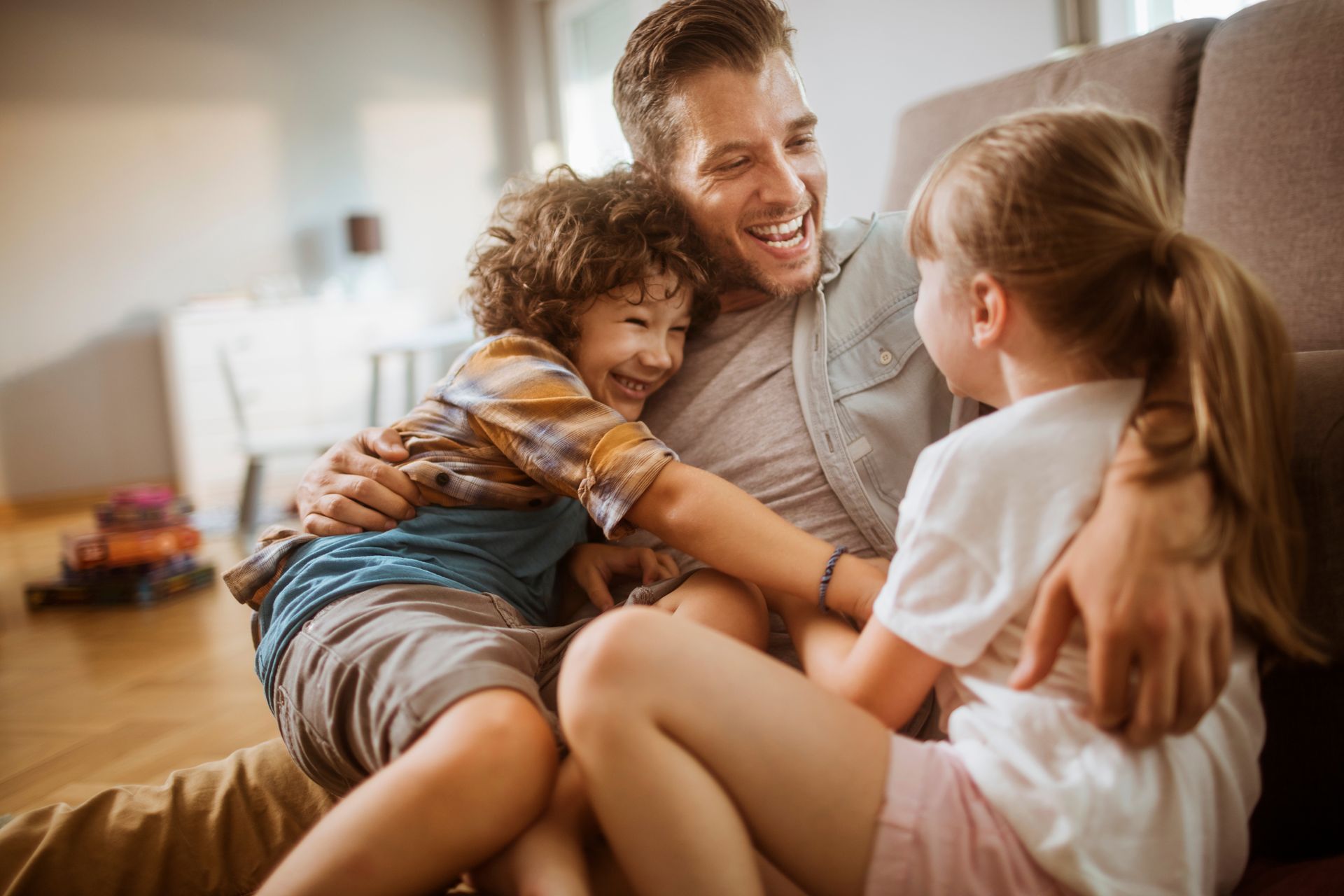 Man laughing with two children, embracing, on a couch.