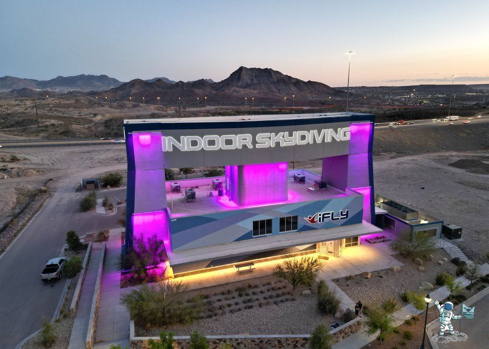 Drone shot of iFly El Paso at night, showcasing neon-colored lights illuminating the building and surrounding area.