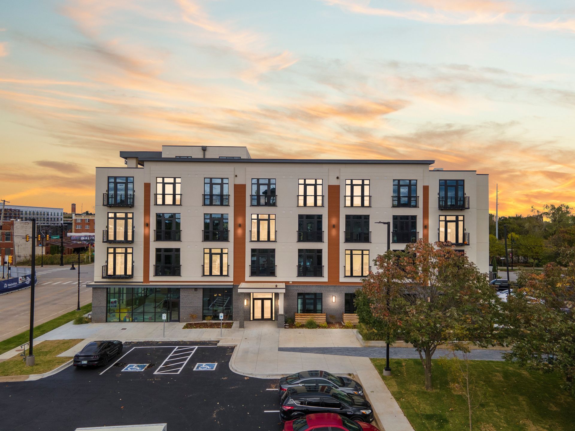 Modern apartment building exterior with parking. Evening sky with orange and yellow hues.