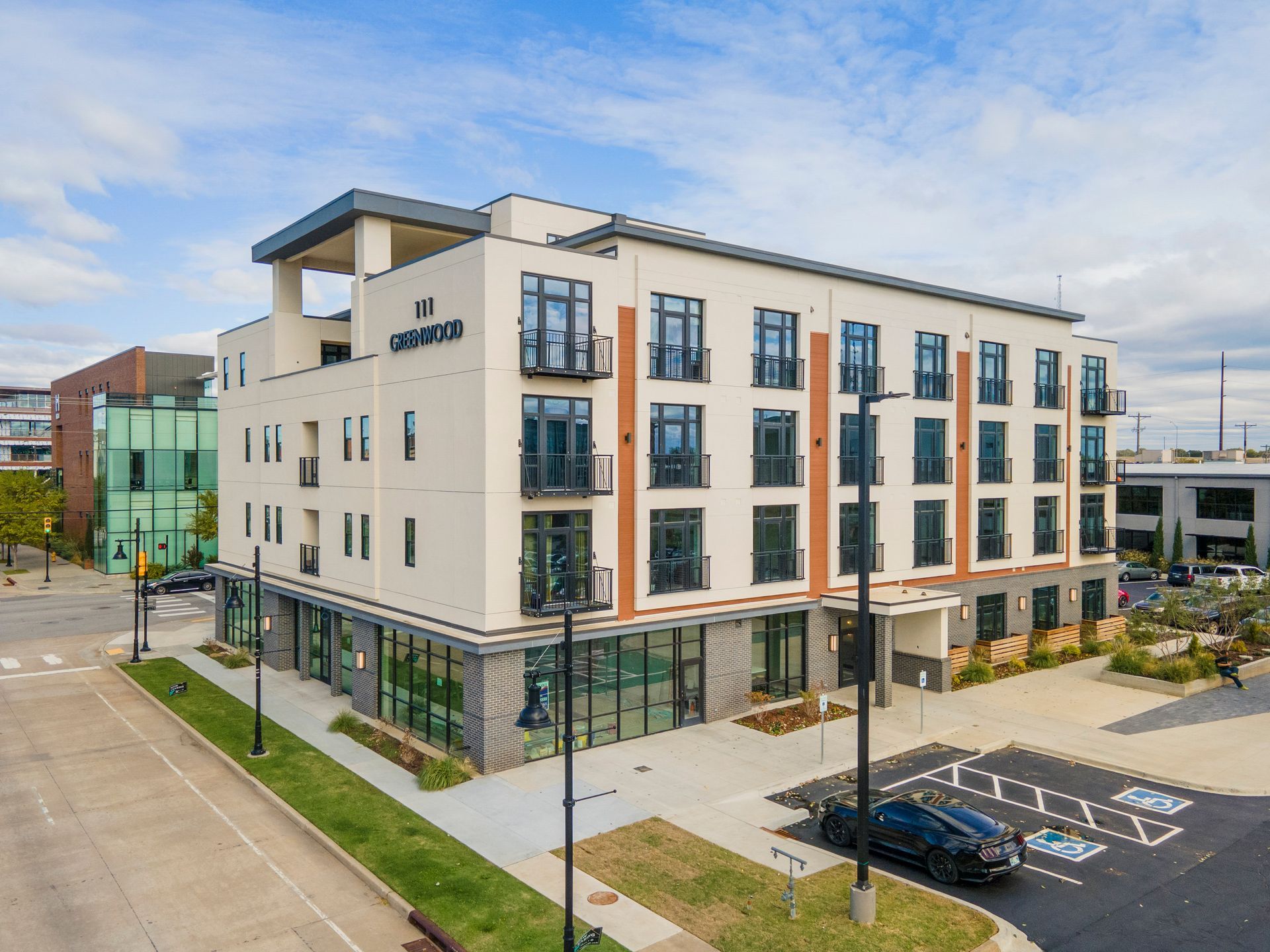 Modern multi-story building with commercial spaces on the ground floor. A black car sits in a parking space.