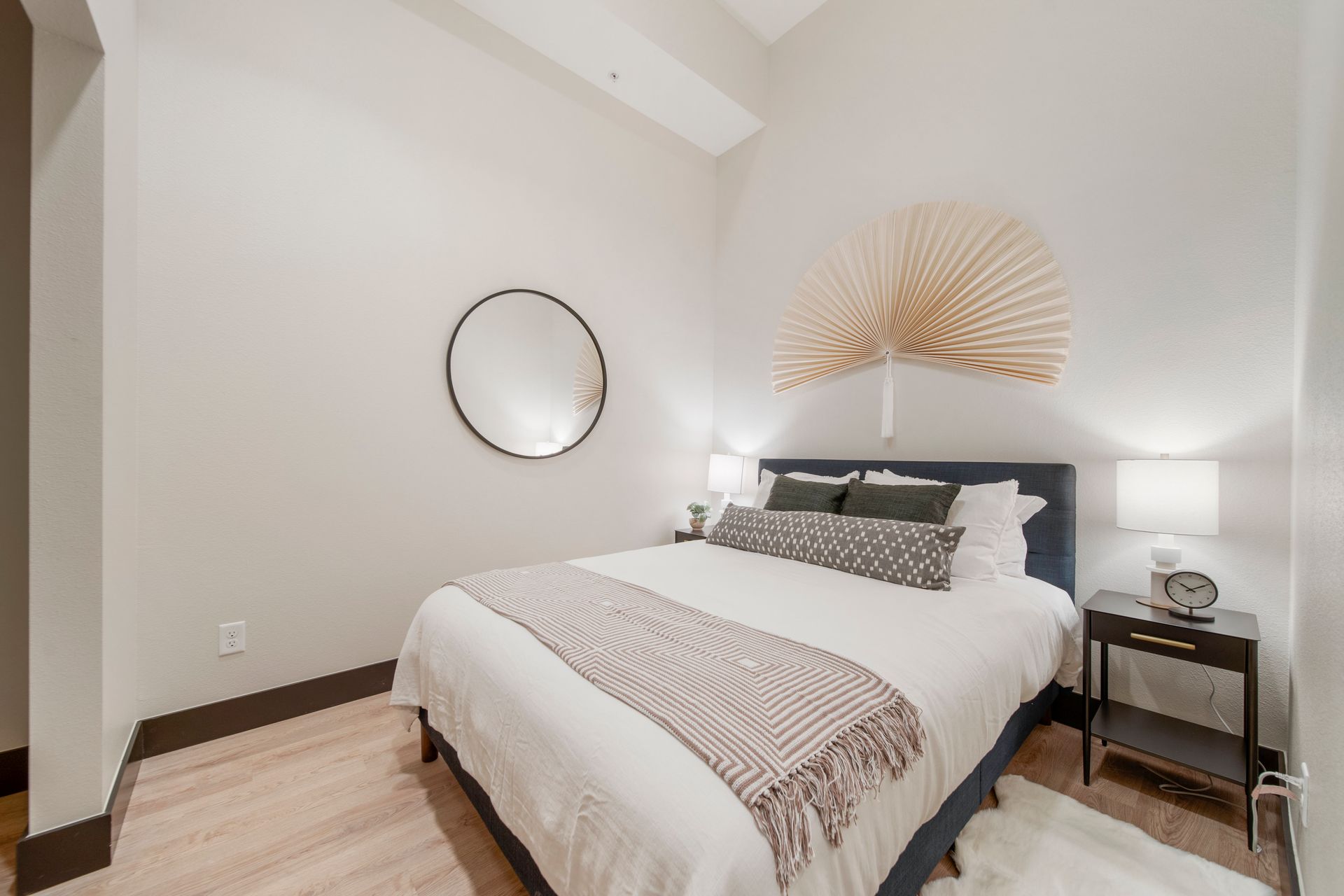 Bedroom with a bed, a round mirror, and a decorative fan on the wall.