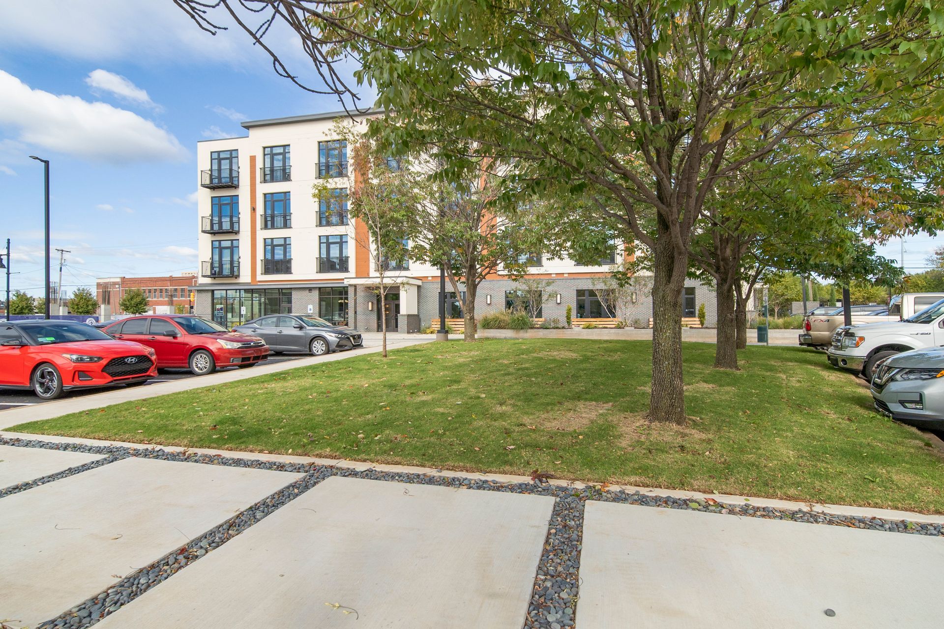 Modern apartment building with cars parked nearby, trees and grass.