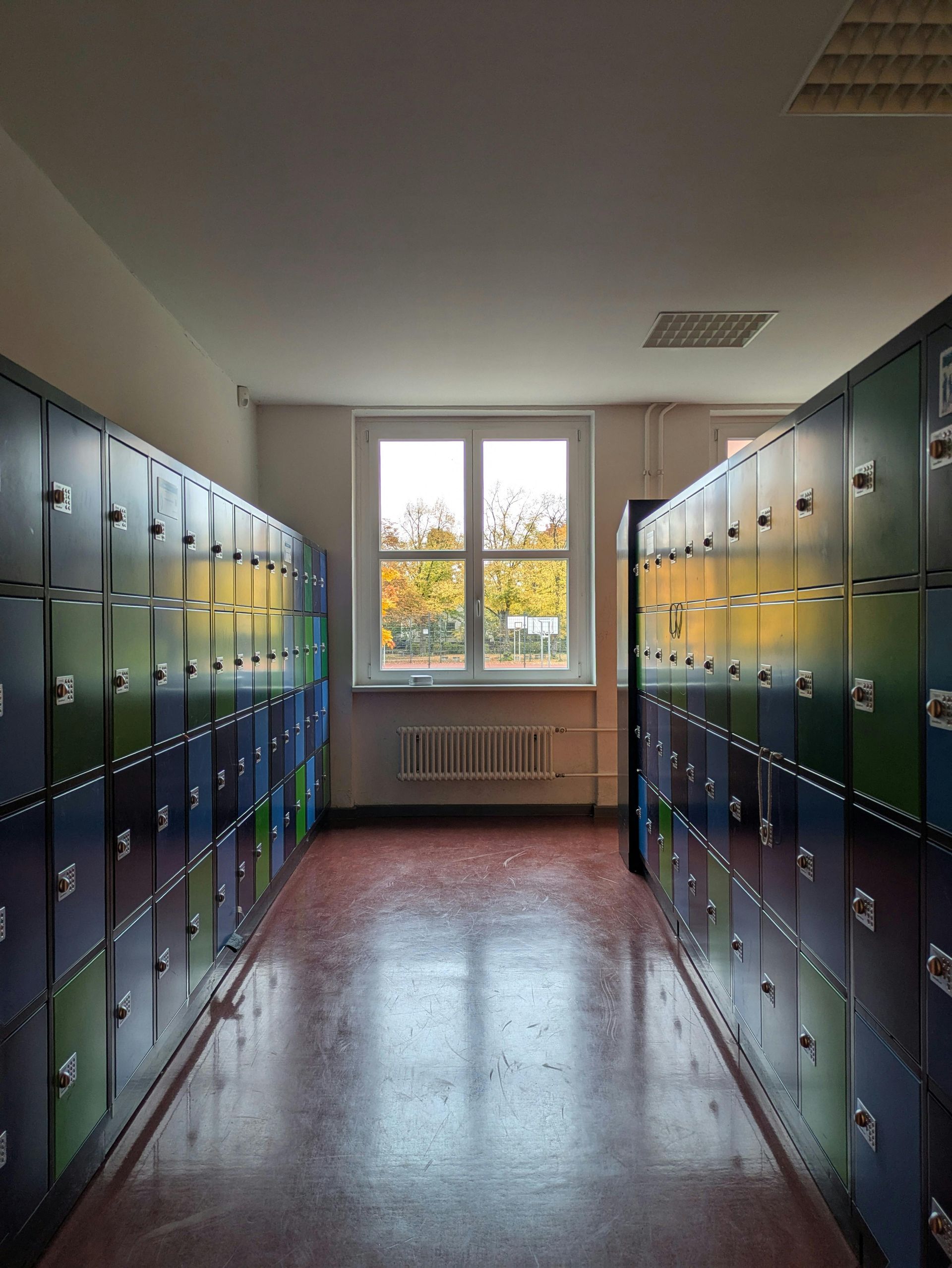 School hallway with rows of lockers, window in the distance. The floor is red, lockers are various colors.