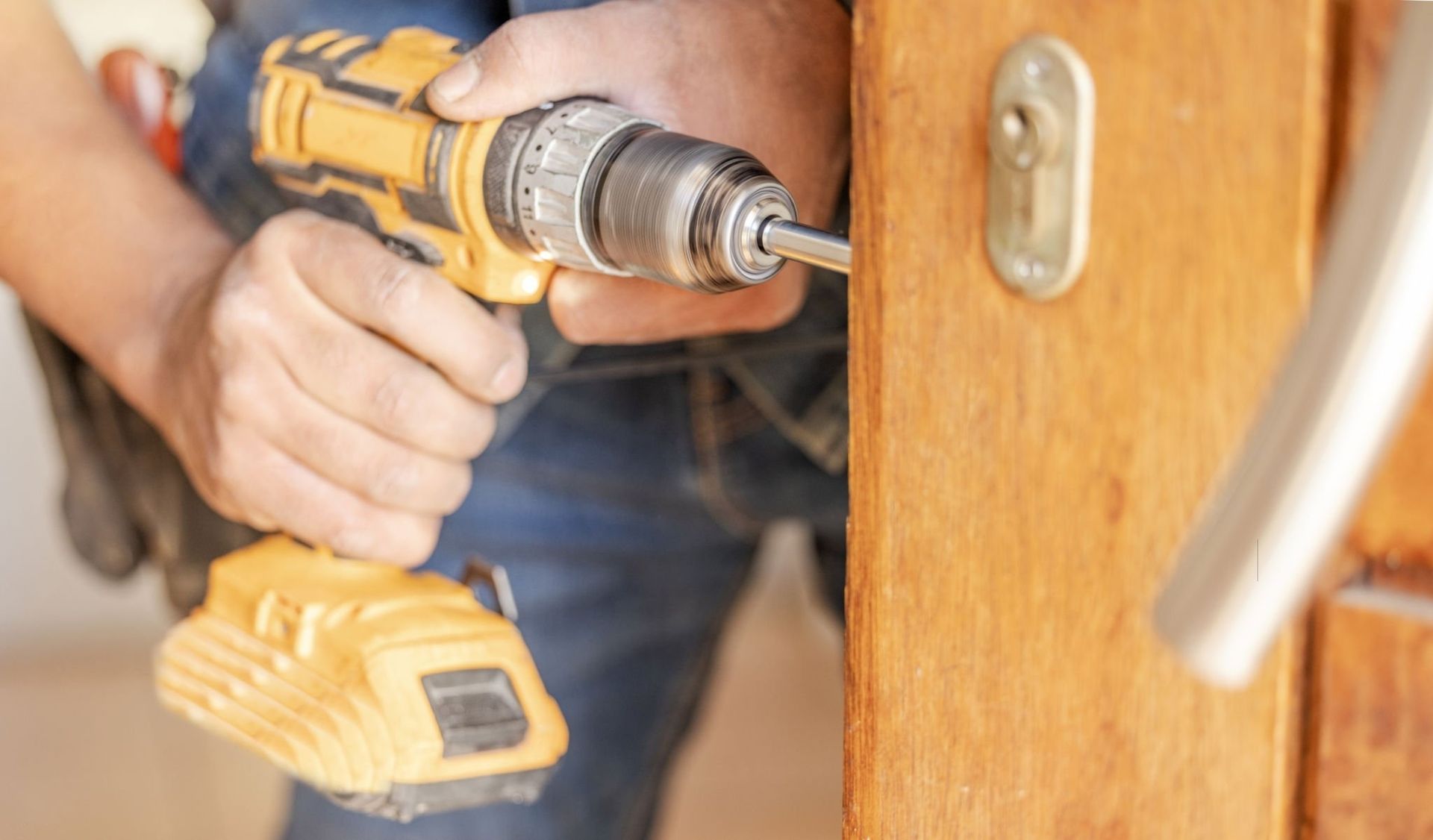 A man is using a drill to fix a door.