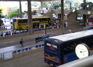 Homem na sala de controle falando ao telefone, supervisionando ônibus estacionados ao ar livre sob abrigo.