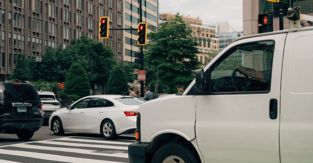 A white van is driving down a city street next to a car.