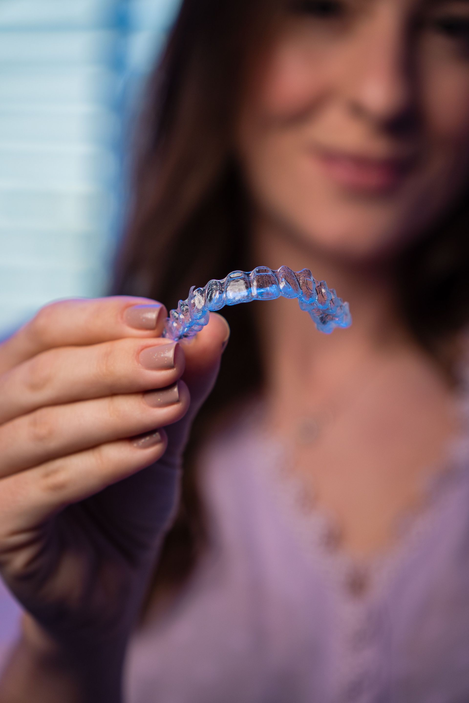 Donna che mostra un apparecchio dentale trasparente verso la fotocamera in un ambiente interno con luce soffusa