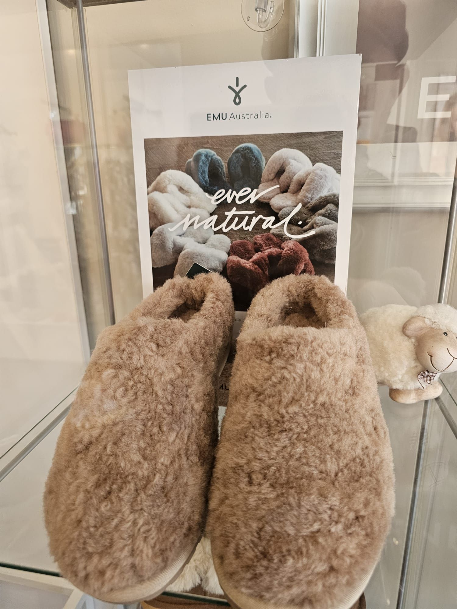 A pair of slippers sitting on top of a glass shelf next to a sheep.