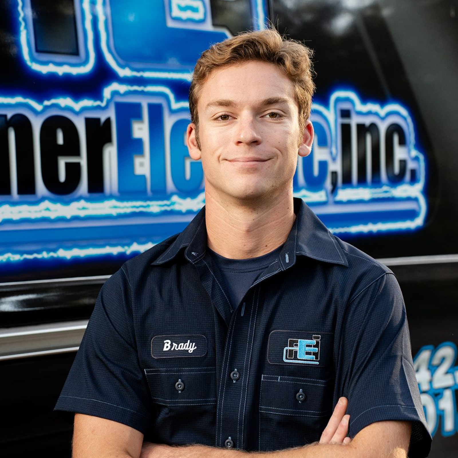 A young man is standing in front of an electric inc. van.