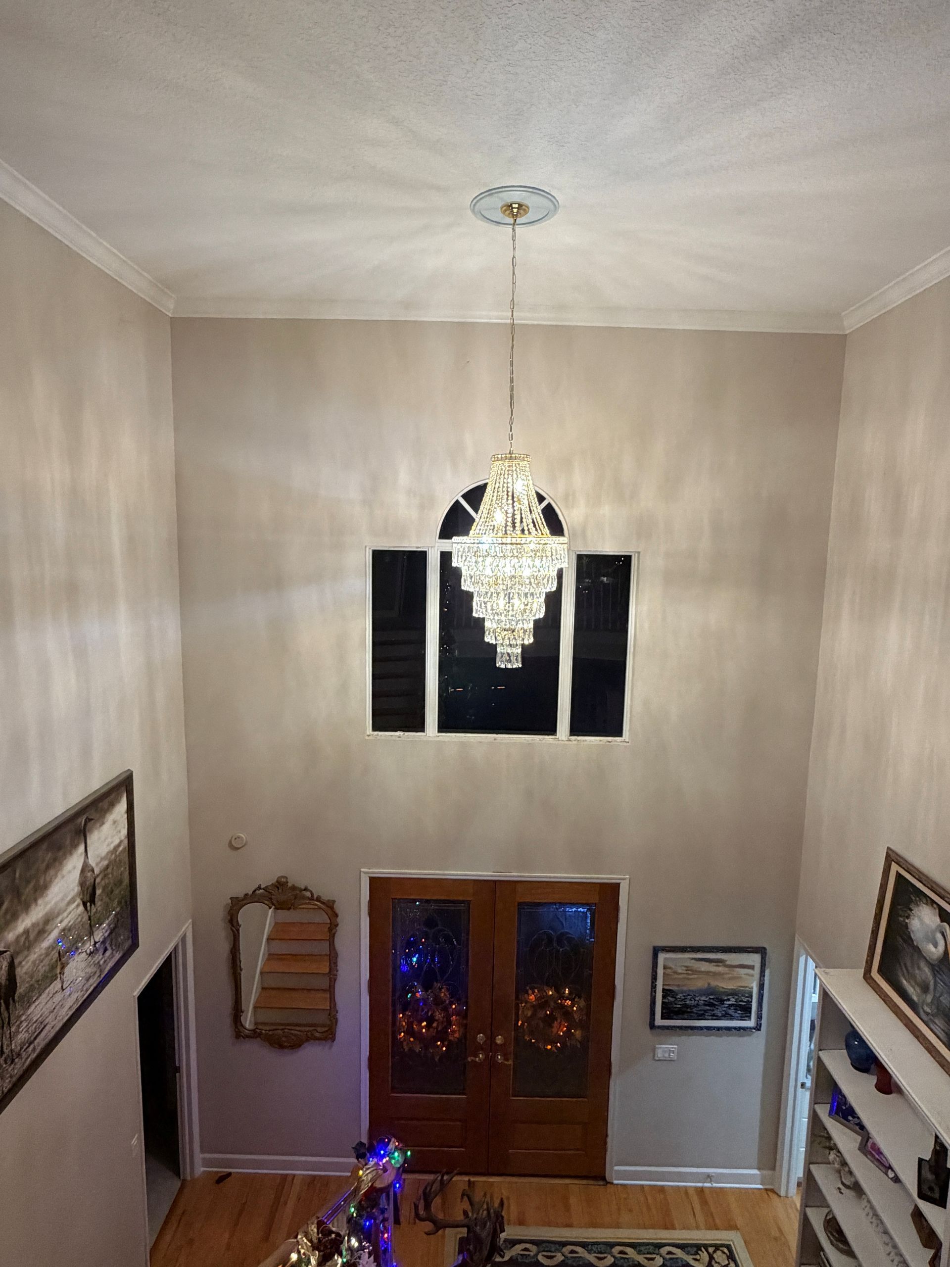 Tall foyer with a chandelier, double front doors, and a staircase at the lower left.