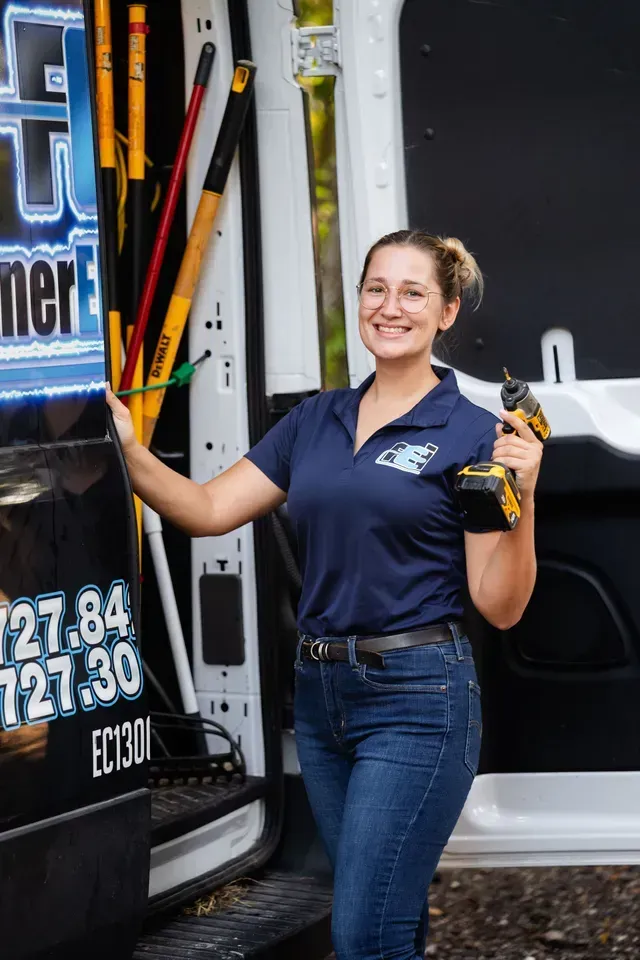 A woman is standing in front of a van holding a drill.
