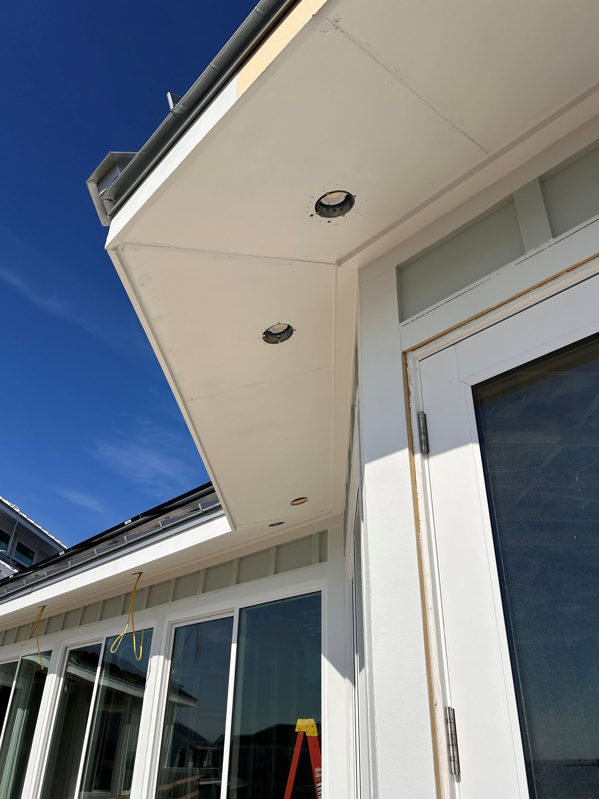 White house eaves with recessed lights and large windows against a bright blue sky