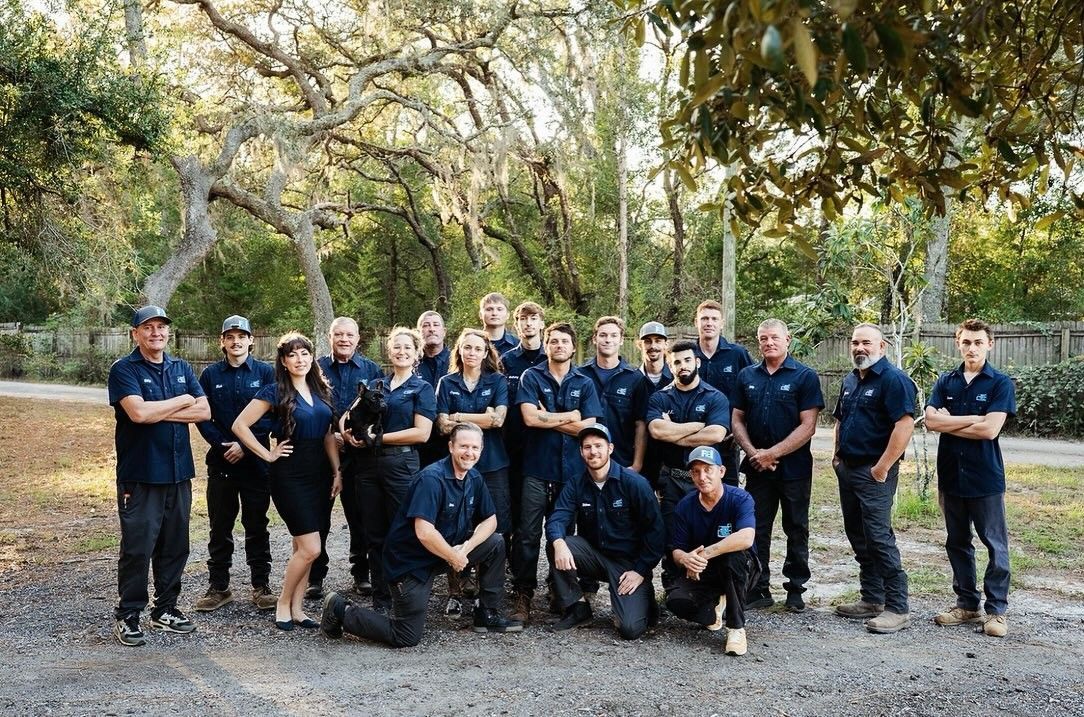 Group of uniformed Faulkner Electric employees posing outdoors on a gravel path under trees