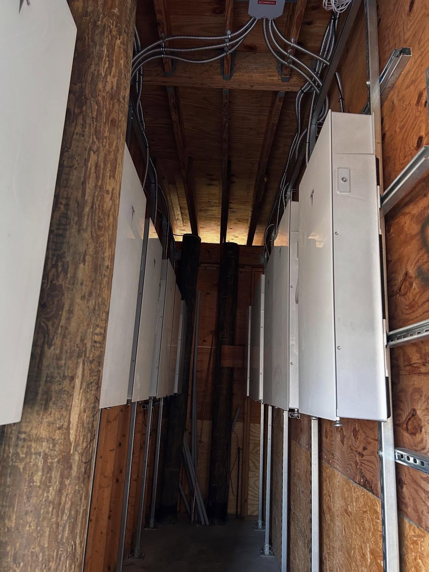 Narrow unfinished corridor with exposed wiring, wooden beams, and white wall panels on both sides