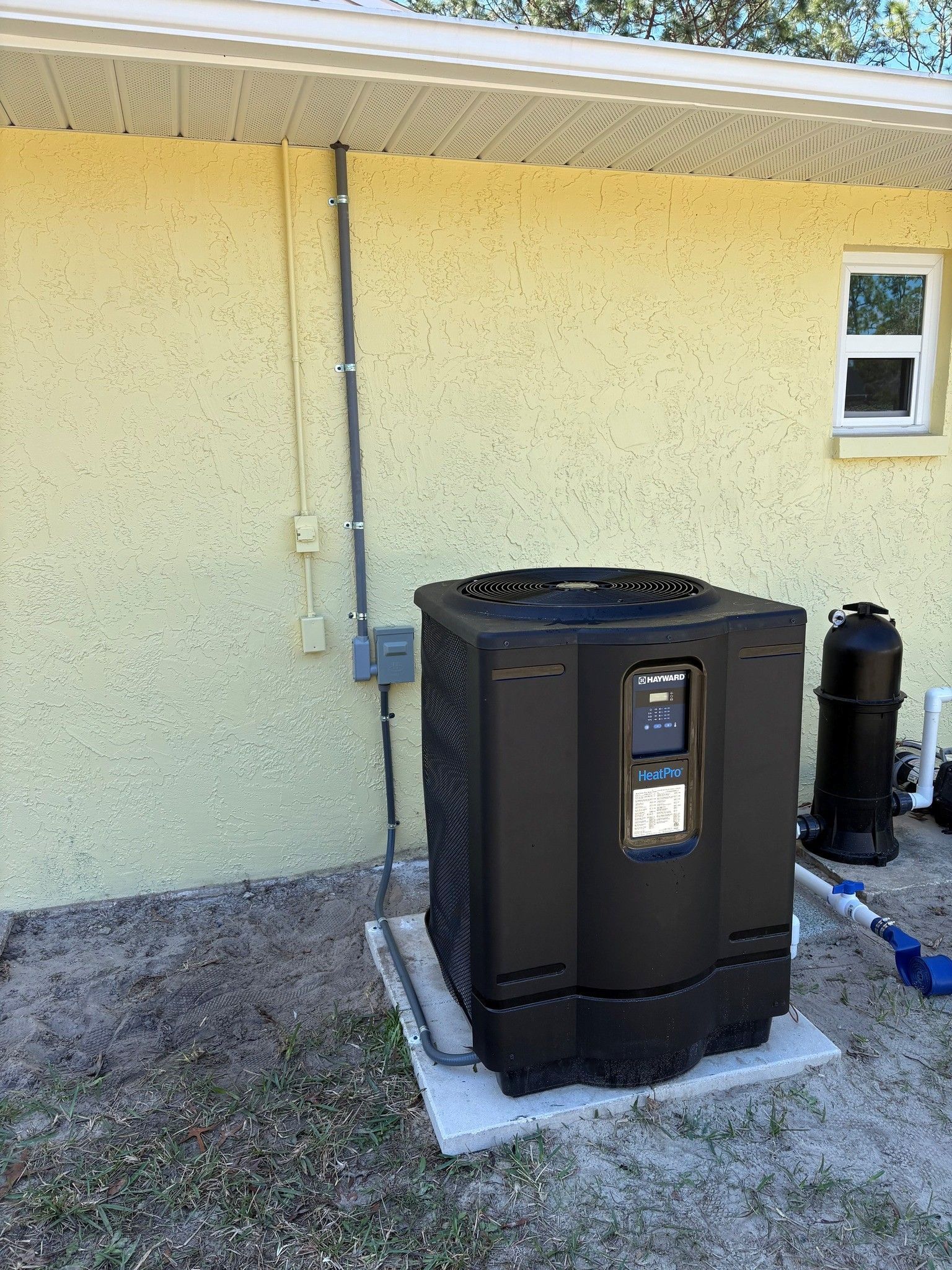 Electrician installing pool heat pump wiring and disconnect box on exterior home wall
