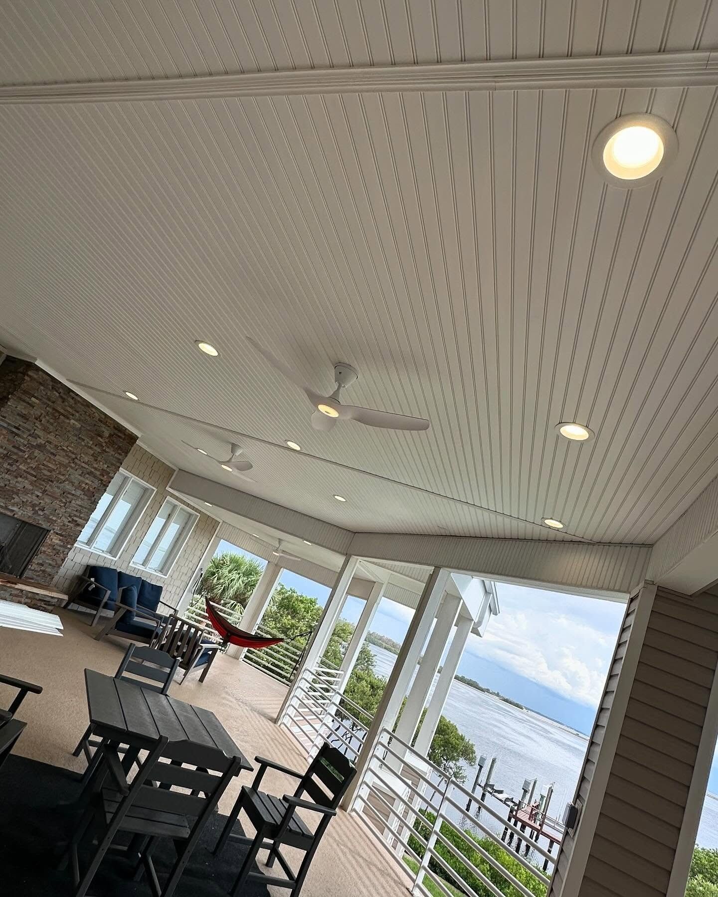 Covered patio dining area overlooking a lake with tables, chairs, and ceiling lights.