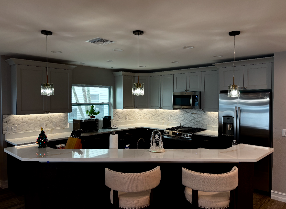 Modern kitchen with white island, pendant lights, stainless steel appliances, and mirrored backsplash