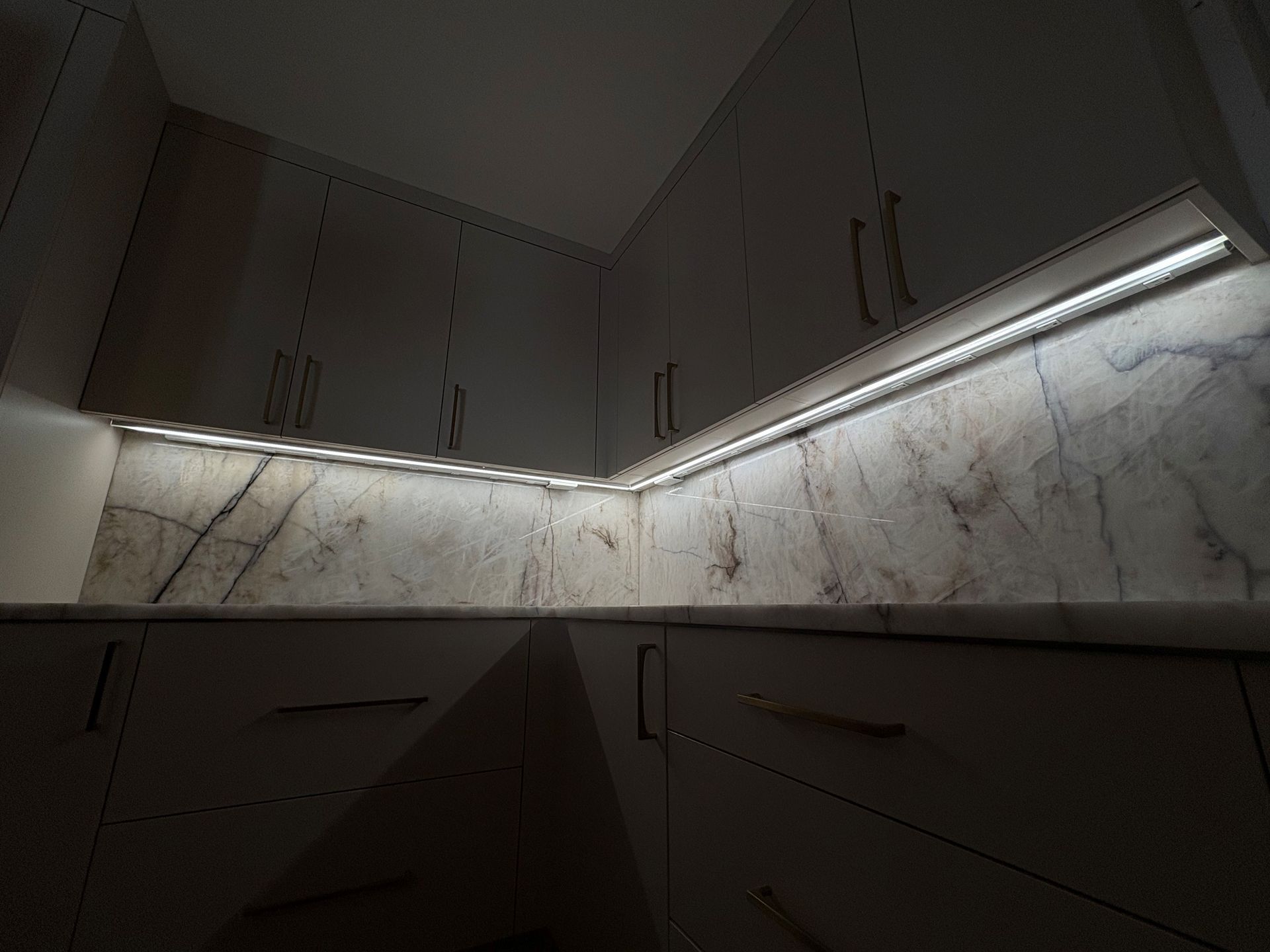 Modern kitchen corner with marble backsplash, white cabinets, and under-cabinet lighting