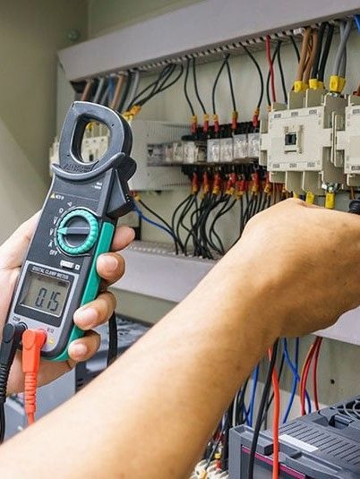 A person is holding a digital clamp meter in their hand.